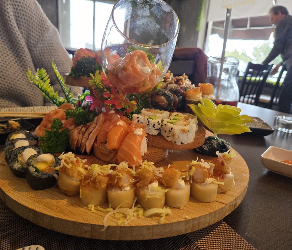Grande tábua de sushi com sashimi, makis e peças crocantes, decorada com flores, na sala do Koen Sushi