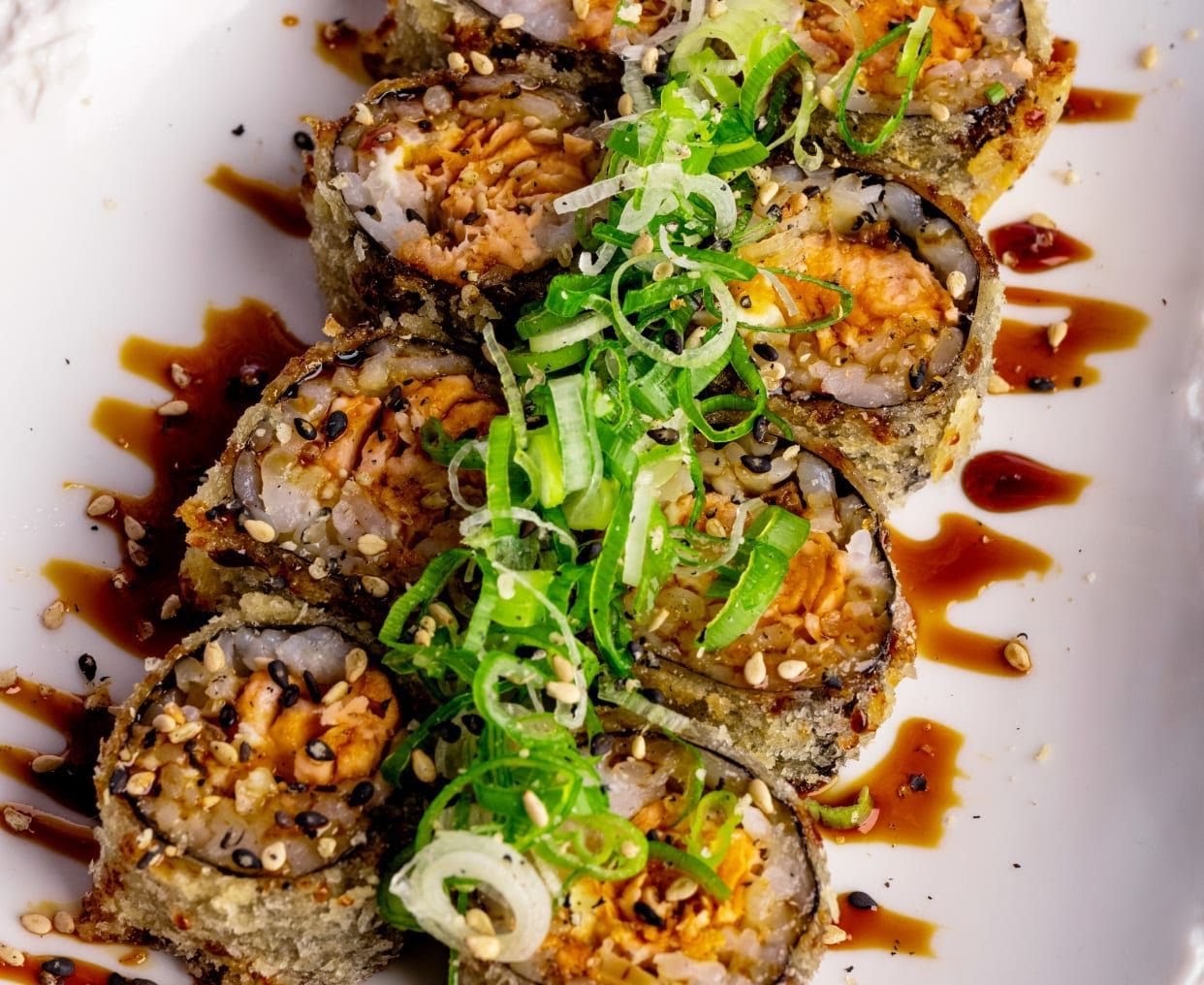 Hot roll panado com salmão, alho-francês e molho teriyaki num prato branco