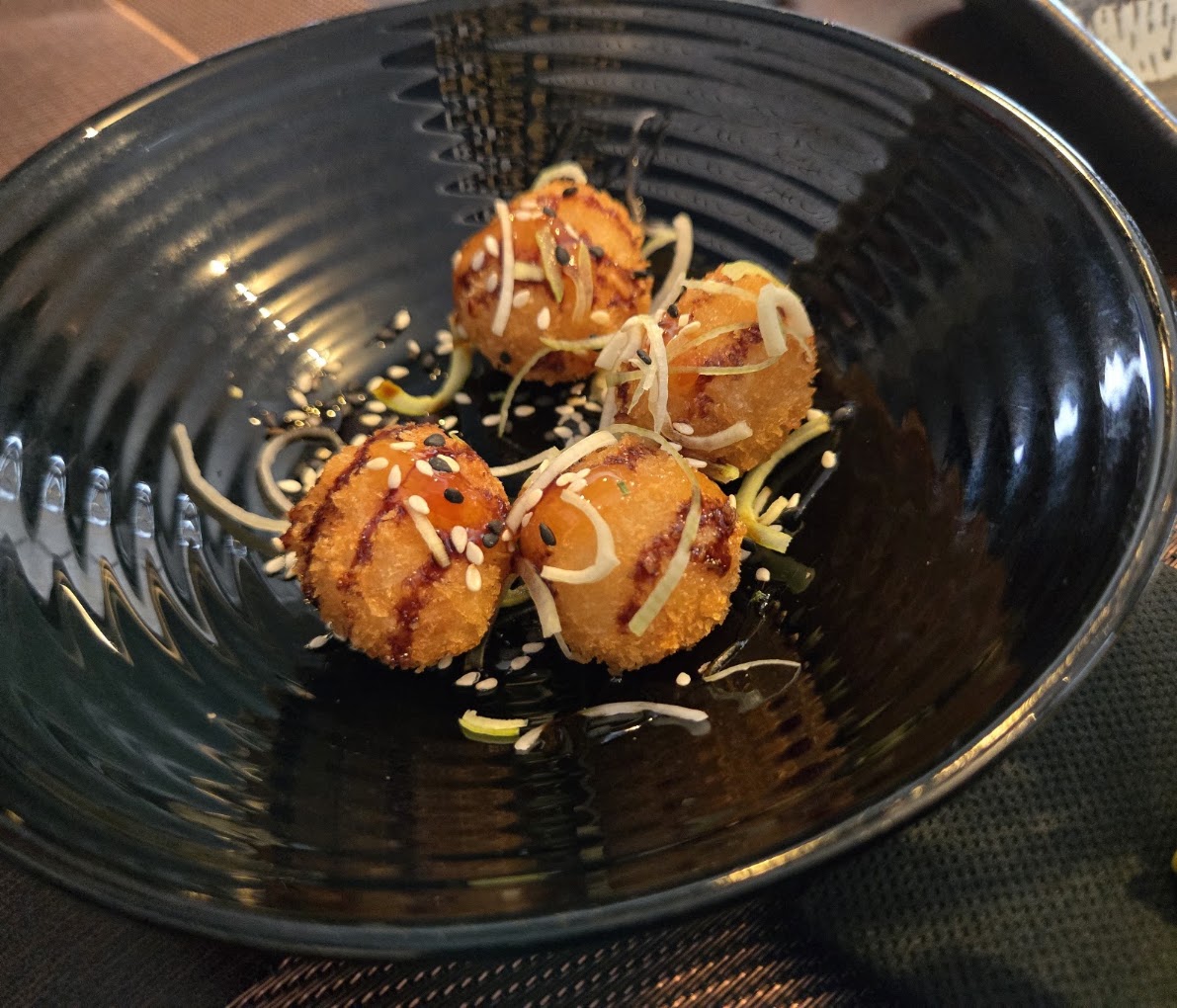 Quatro croquetes crocantes com molho, sésamo e alho-francês, numa taça preta