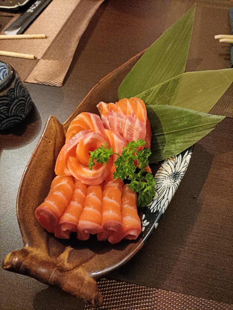 Sashimi de salmão em rolinhos e em flor, servido num prato de cerâmica em forma de folha