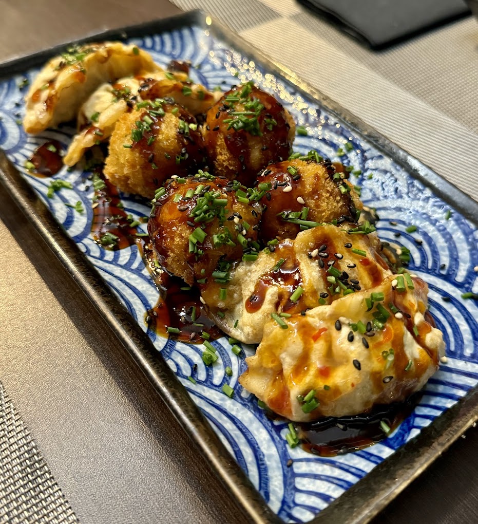 Gyozas e croquetes crocantes com molho e cebolinho, num prato azul com padrão de ondas