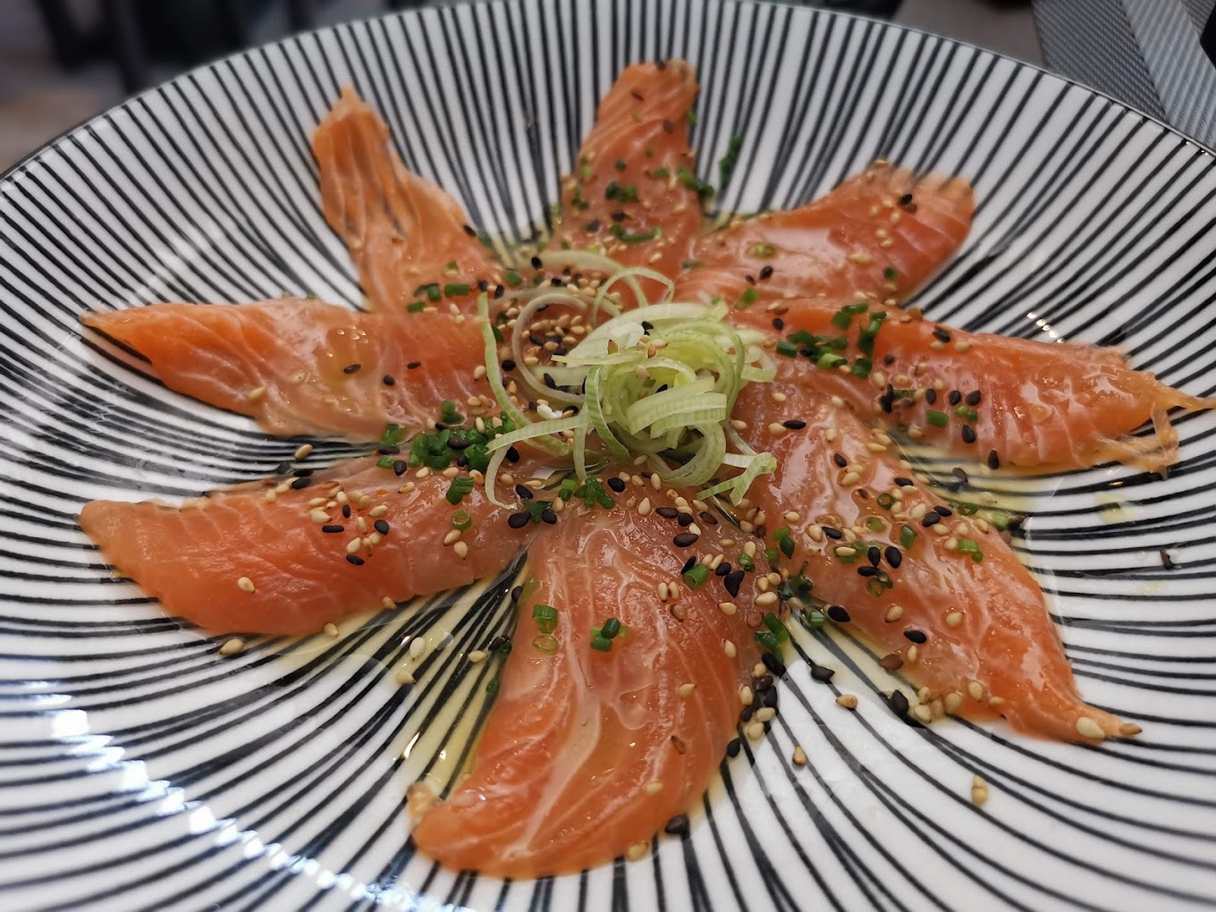 Sashimi de salmão disposto em estrela com sésamo e cebolinho, num prato listado a preto e branco